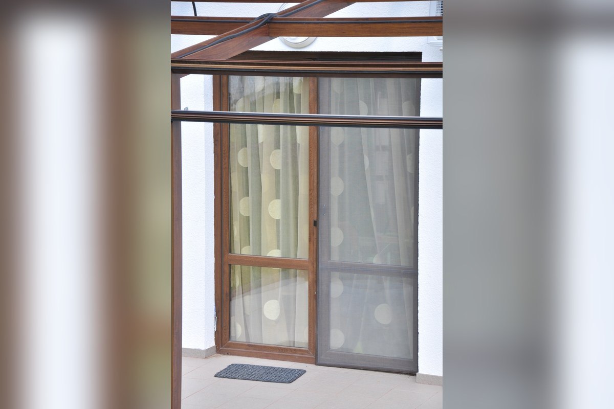 Ușă de terasă cu o plasă antiinsecte care culisează lateral, lângă un canat cu perdea